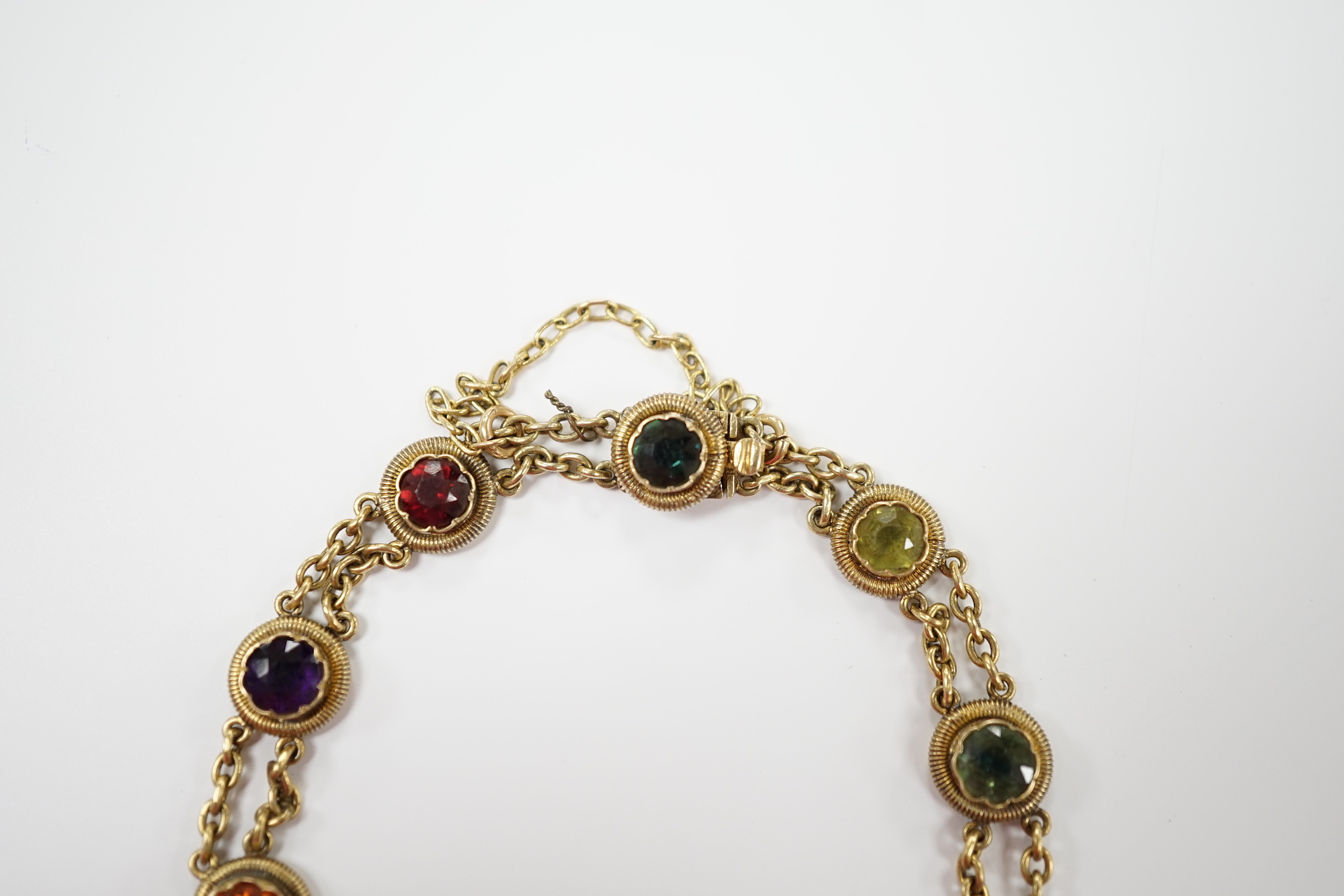 An early 20th century yellow metal (stamped 15 and also 9??) and ten stone multi gem set chain link bracelet, 16cm, gross weight 14.6 grams, the stones include amethyst, hessonite garnet and tourmaline.